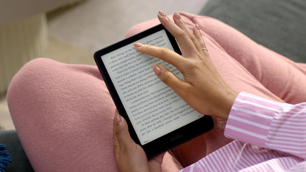 A person reads on an Amazon Kindle Paperwhite Signature Edition while relaxing in cozy clothes.