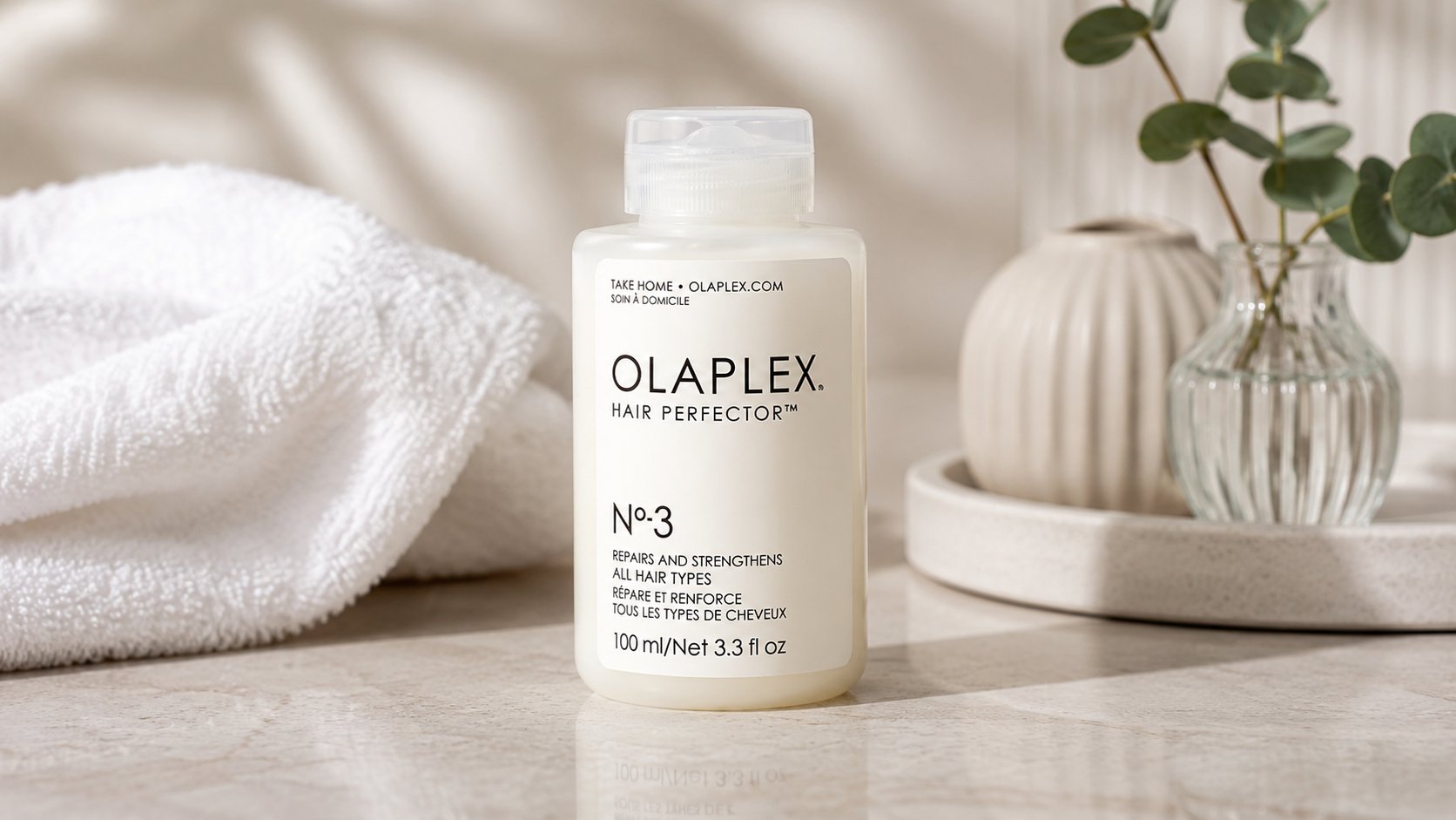 Olaplex No. 3 Hair Perfector bond repair treatment bottle on a marble bathroom countertop with soft natural lighting, towel, and eucalyptus décor for damaged hair care.