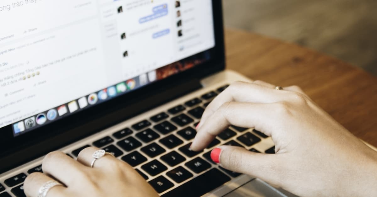 Hands typing on laptop keyboard while messaging online on a social media platform